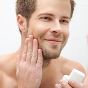 joven poniéndose crema facial antiarrugas para hombre