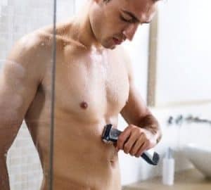 hombre usando una afeitadora corporal bajo la ducha